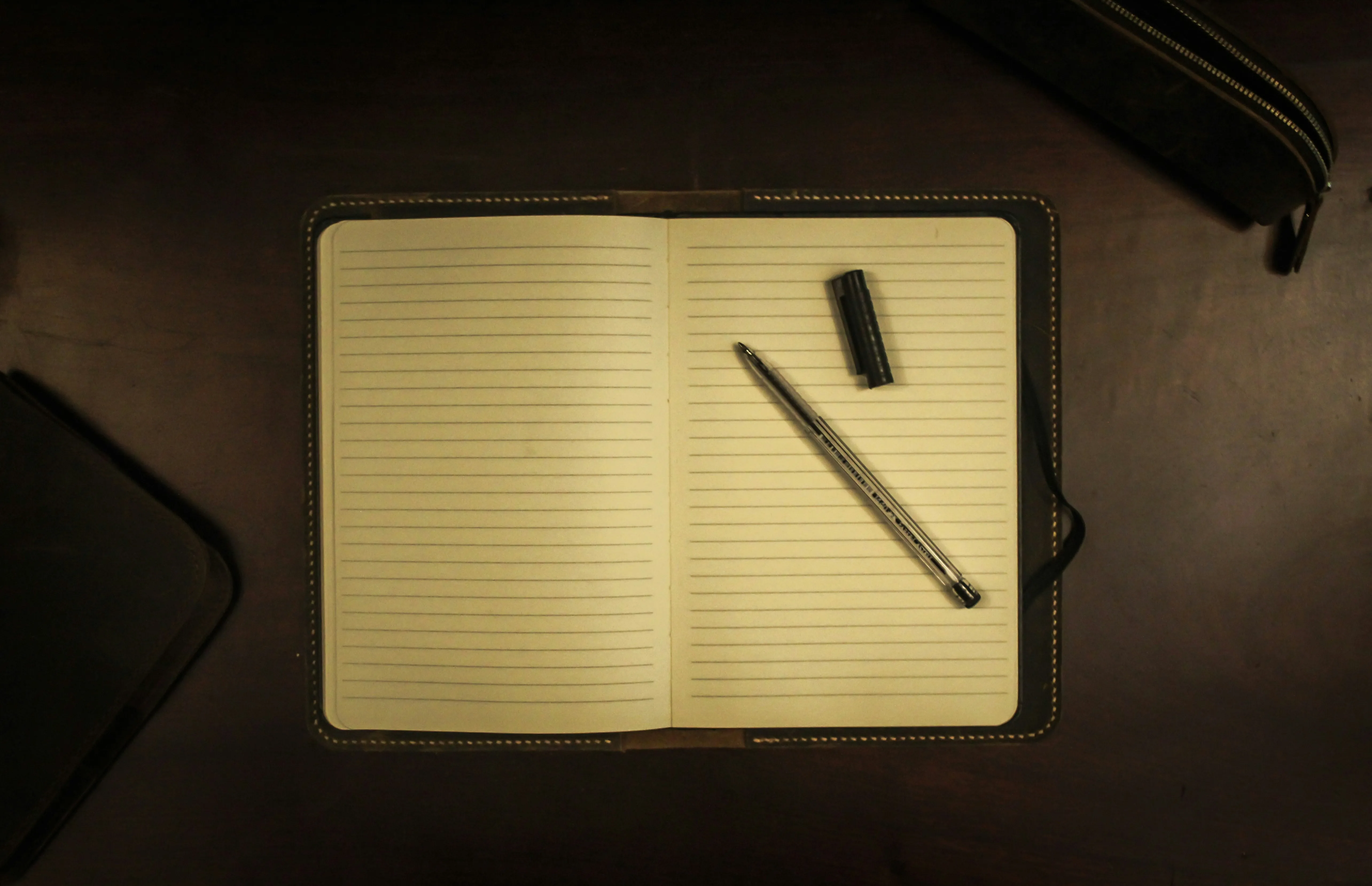 Open notebook with a pen on a dark wooden desk, symbolizing the initial steps on how to set up Python logging module with file handlers and message formatting.