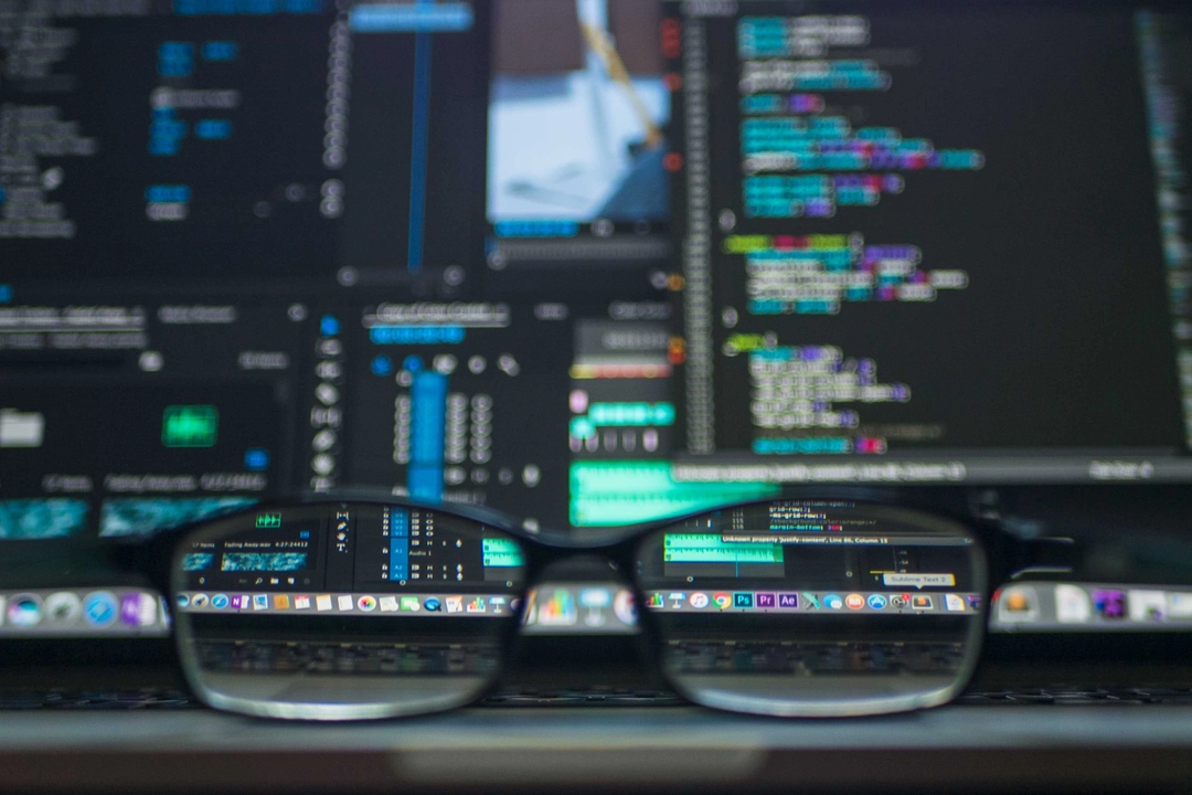 Close-up of eyeglasses focused on computer screens displaying code, illustrating the concept of Python functors and monads for efficient programming.